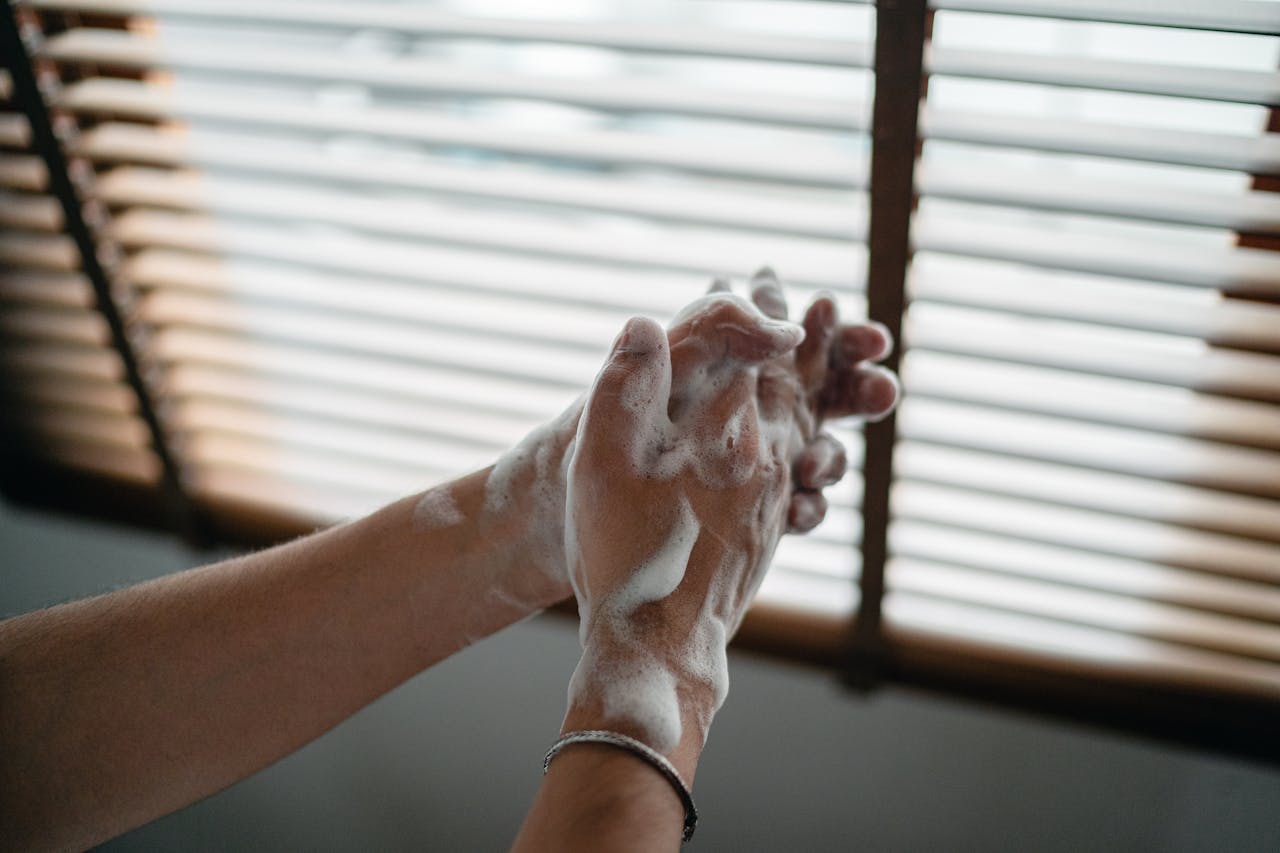 services-02 Hands covered in soap lather being washed indoors near a window for hygiene.